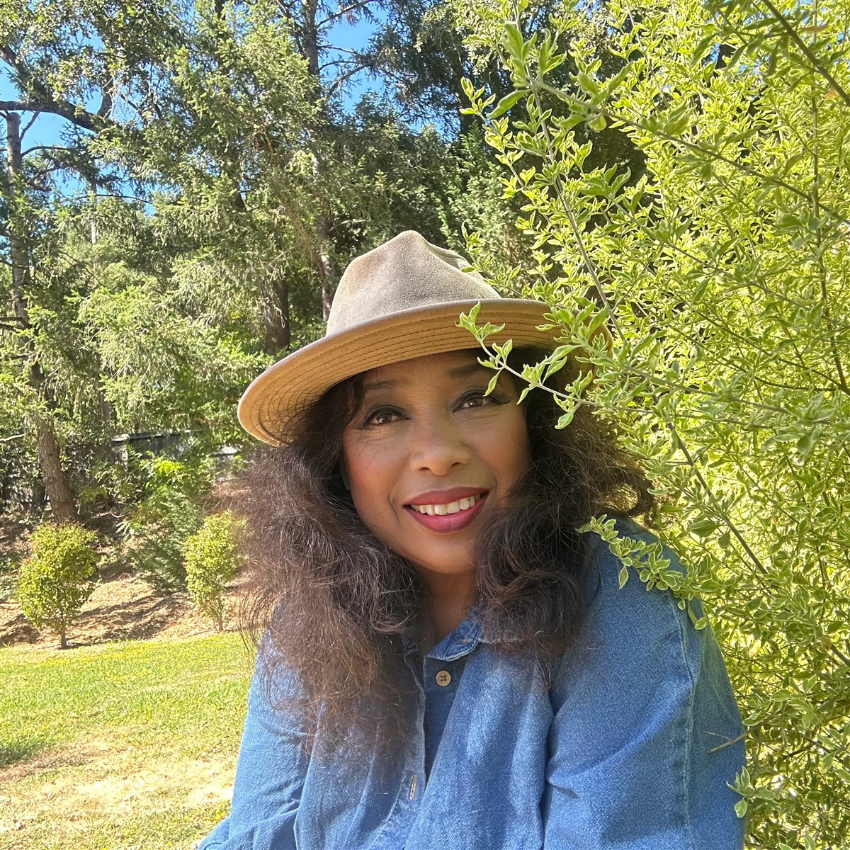 Michelle in a wide-brimmed hat among green trees